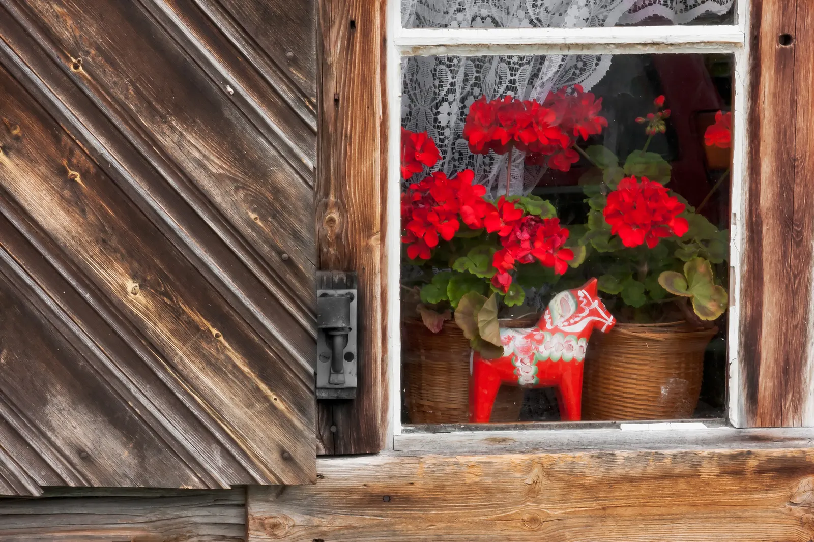 Röd dalahäst och röda pelargoner i fönstret till en gammal timmerstuga