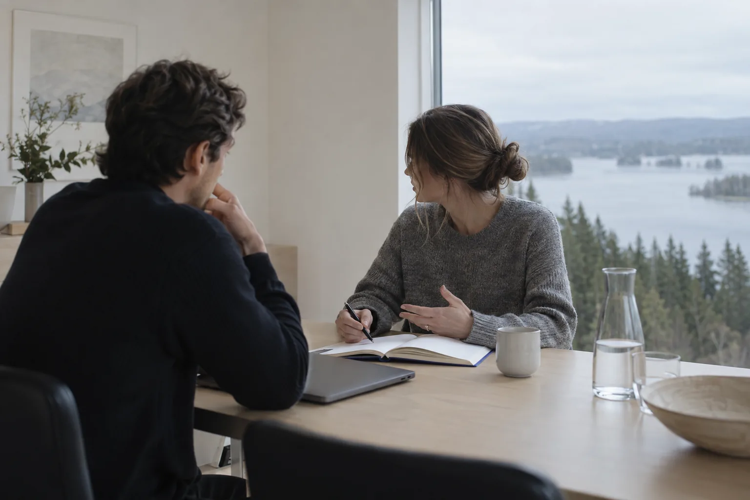 Two people in a meeting by a window overlooking a lake and forest